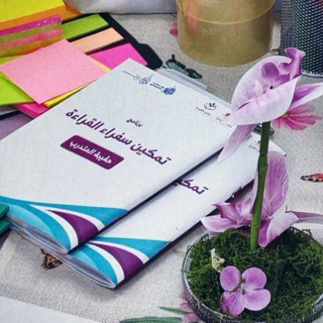 حقيبة المتدرب لبرنامج تمكين سفراء القراءة على طاولة التدريب، وبجوارها زهرة أوركيد